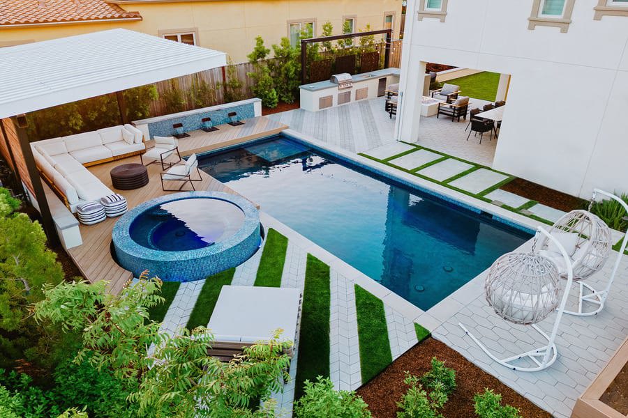 A backyard with multiple linear designs created using patio pavers, featuring a pool, dining area and sitting area.