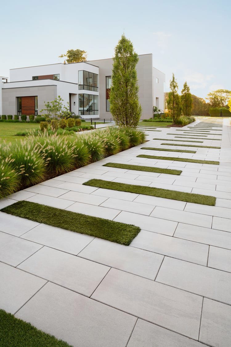 A walkway outside of a house that uses spaces between the pavers to create strips of grass.