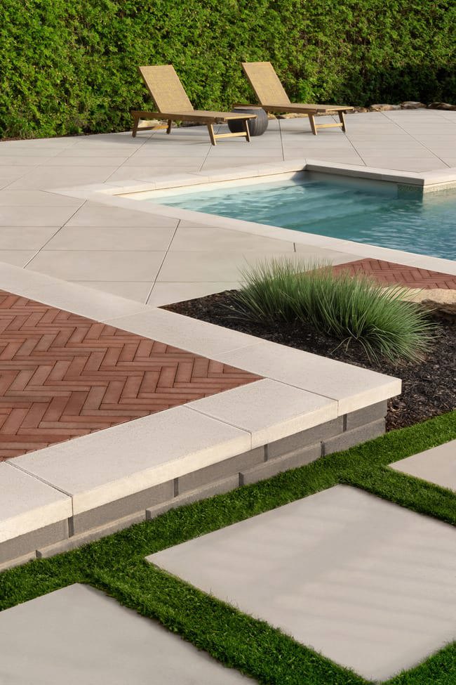 Patio corner featuring a paver installed in a herringbone pattern with a cream colored stone boarder.